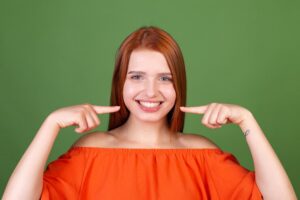 young-red-hair-woman-casual-orange-blouse-green-wall-point-fingers-white-teeth-perfect-smile_343596-6943