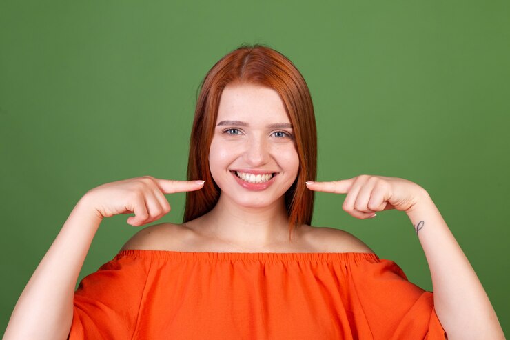 young-red-hair-woman-casual-orange-blouse-green-wall-point-fingers-white-teeth-perfect-smile_343596-6943