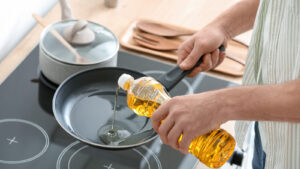 Man,Pouring,Sunflower,Oil,On,Frying,Pan,In,Kitchen