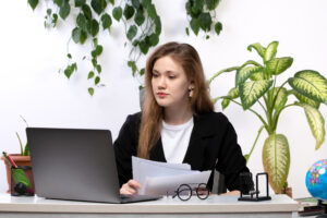 front-view-young-beautiful-lady-white-shirt-black-jacket-working-with-documents-using-her-laptop-front-table-with-leaves-hanging